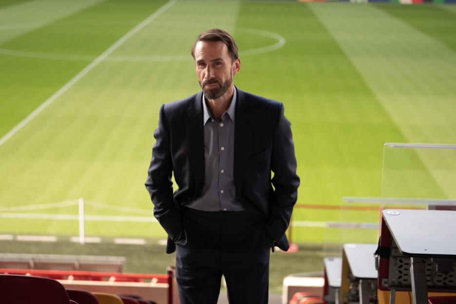 Gareth Southgate (Joseph Fiennes) standing in an empty football stadium.