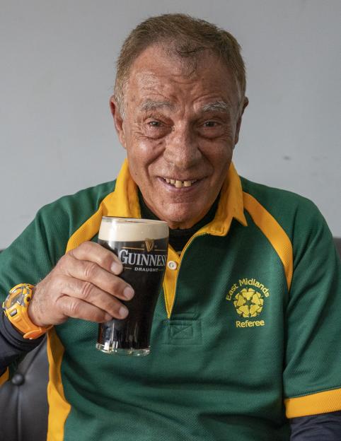 Britain's oldest referee, Nando Di Matteo, 87, in a green and gold "East Midlands Referee" shirt, holding a glass of Guinness.
