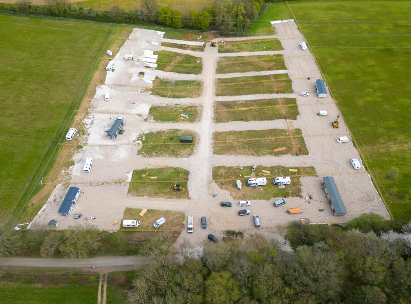 Aerial view of a caravan park under construction, with mobile homes and caravans on gravel plots surrounded by green fields.
