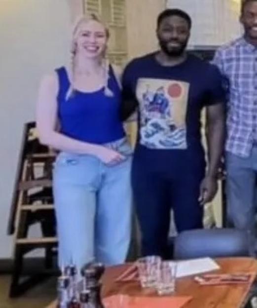 The cast of Traitors, including Ellie and Ross, standing together in a restaurant with a pizza oven.