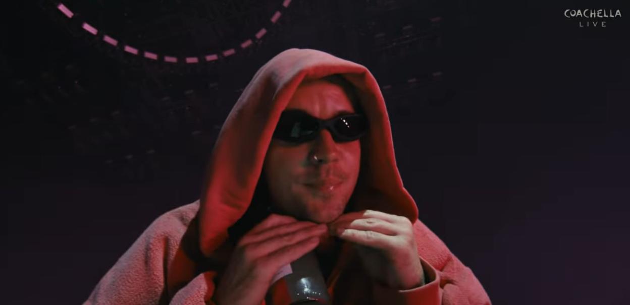 Justin Bieber performing at Coachella, wearing a red hoodie and sunglasses.