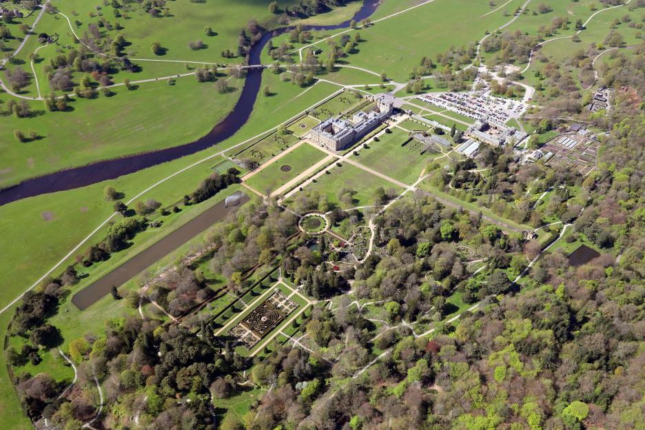 Aerial view of Chatsworth House, its gardens, and surrounding parkland with a river.