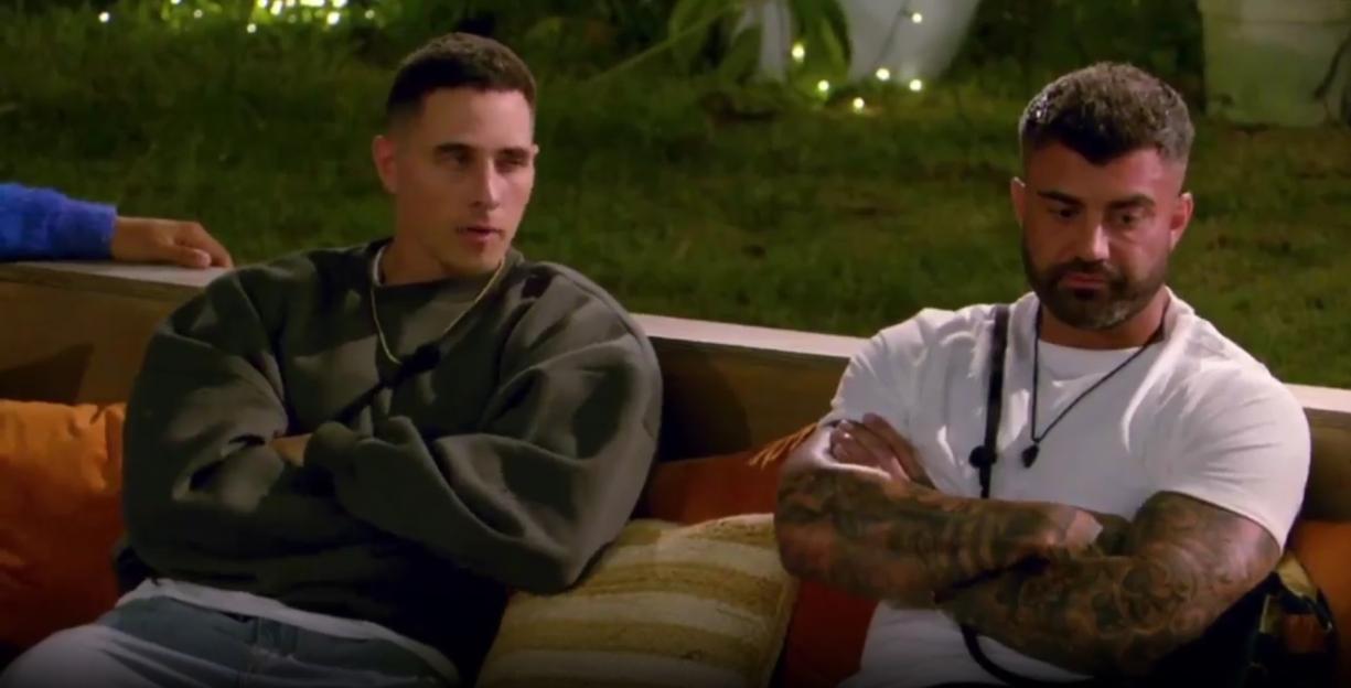 Two men with their arms crossed, sitting on an outdoor sofa.