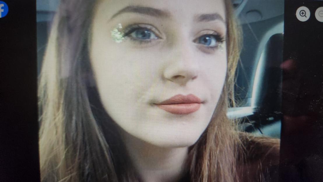 A close-up of a young woman with long hair, wearing light blue contacts and glitter under her eyes.