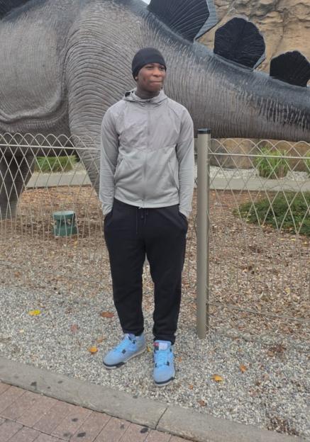 Eghosa Ogbebor standing in front of a Stegosaurus statue.