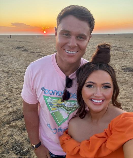 Charlotte Dawson and a man posing for a selfie on a beach at sunset.