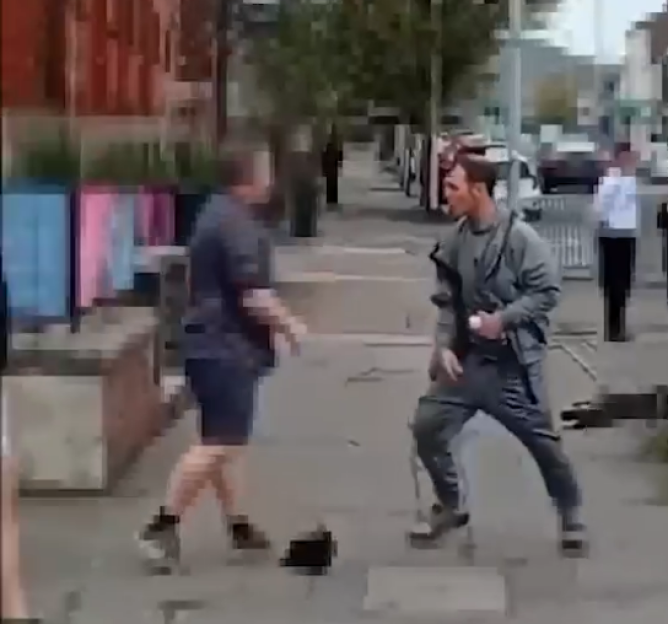 Two men in a physical confrontation on a sidewalk outside a store.
