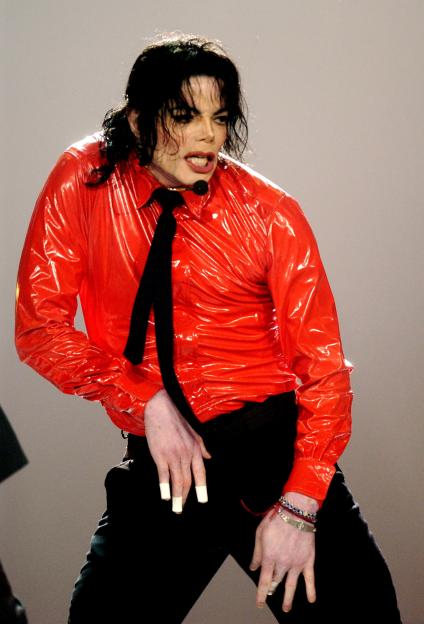 Michael Jackson performing on stage in a red shiny shirt and black tie.