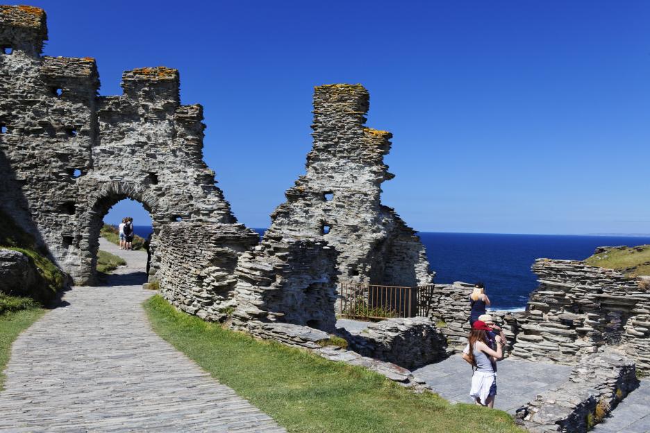 a woman taking a picture of a ruined building overlooking the ocean