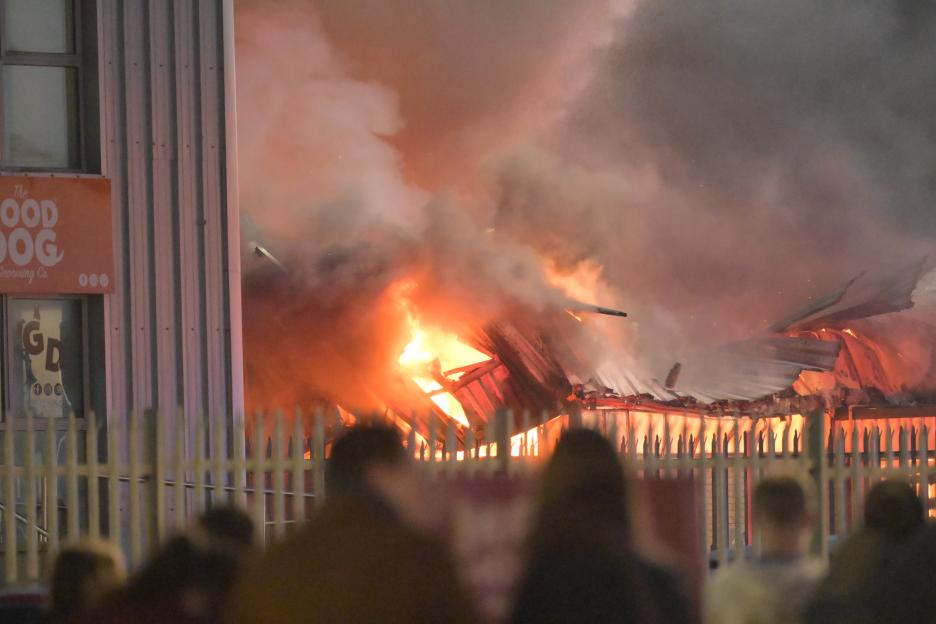 Industrial estate building engulfed in flames with bright orange fire and dense smoke.