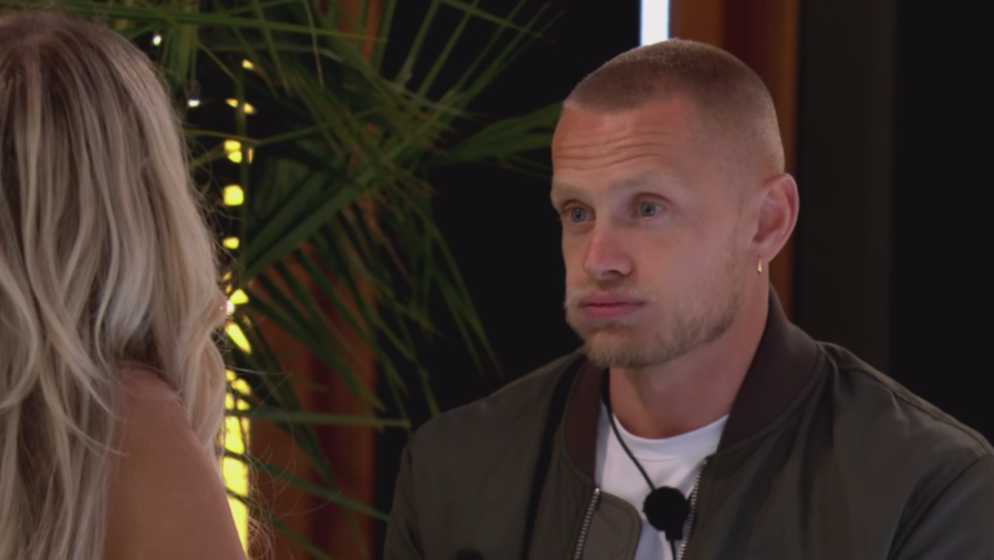 A man with a serious expression and pursed lips looking at a blonde woman.