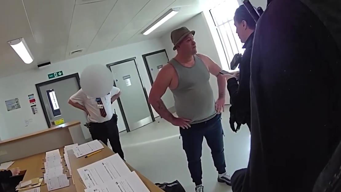 Man wearing a tank top and fedora being arrested by police officers as he leaves prison.