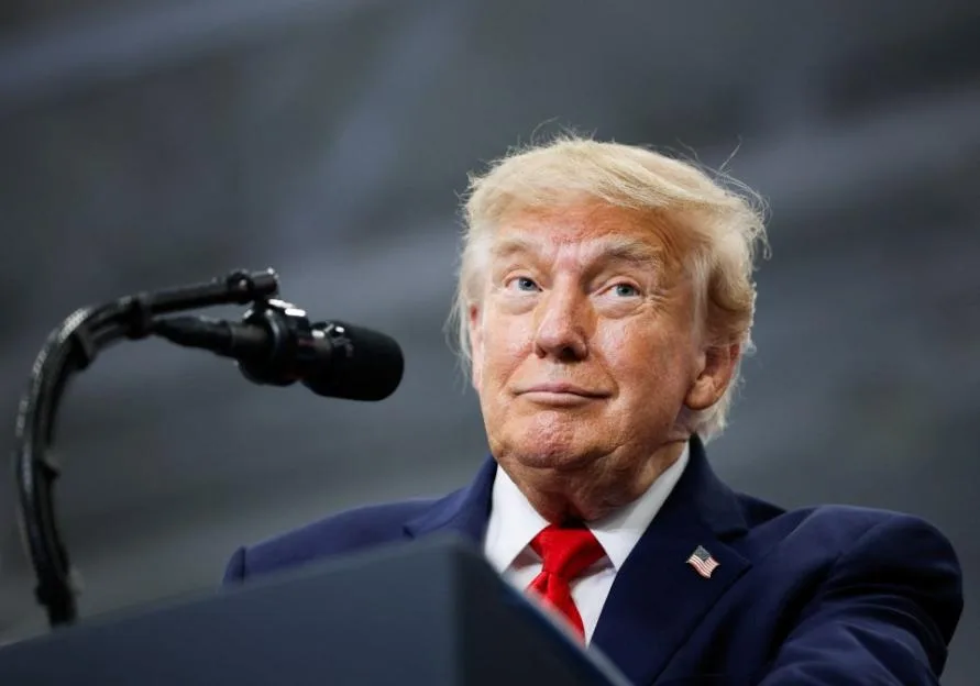 US President Donald Trump speaking at a podium in a blue suit and red tie.