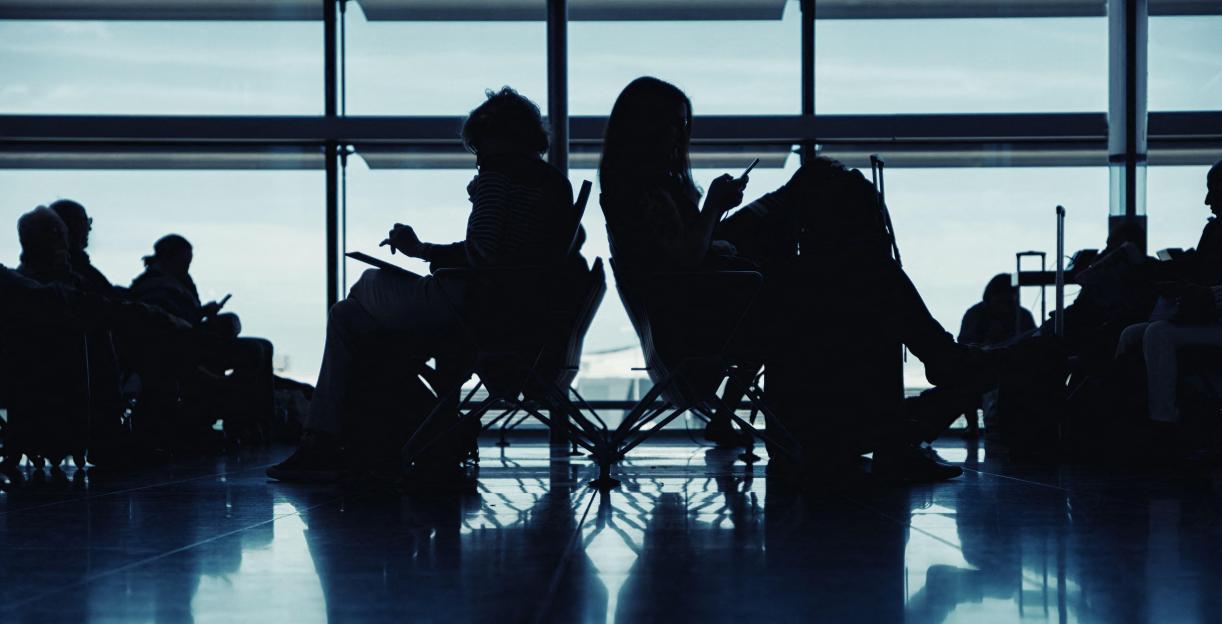 Silhouettes of travelers waiting in an airport terminal.