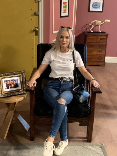 Zoe Hughes sits in a chair in an apartment that appears to be a replica of the Friends TV show set.