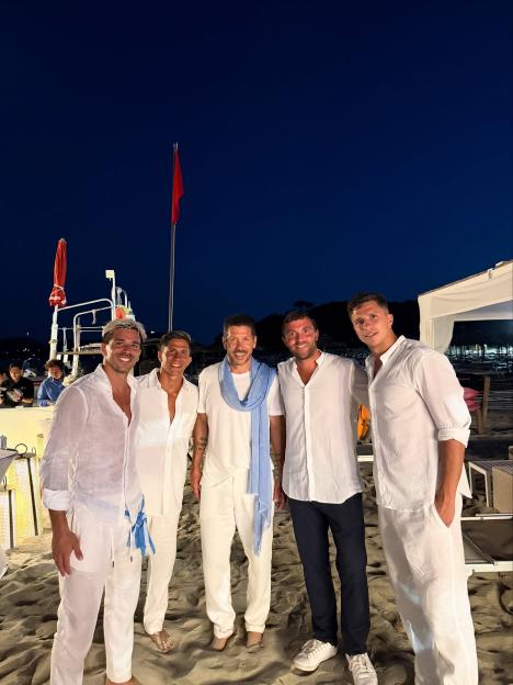 Fabrizio Romano (center, with blue scarf) with four other men on a sandy beach.