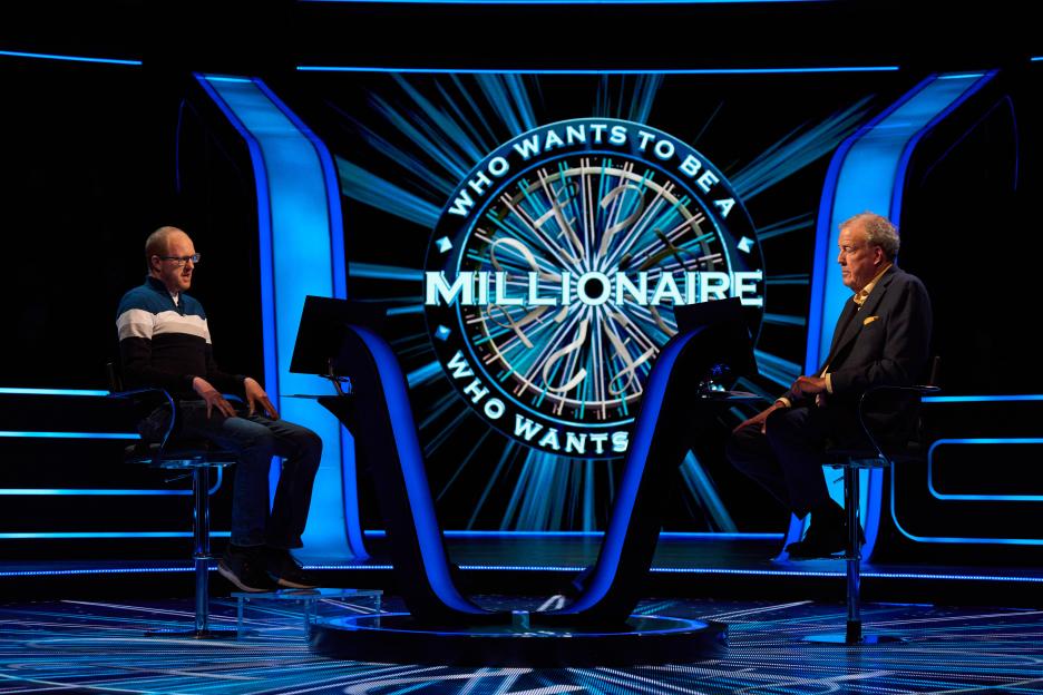 Andrew Fanko and Jeremy Clarkson sitting opposite each other in the "Who Wants to Be a Millionaire" studio.