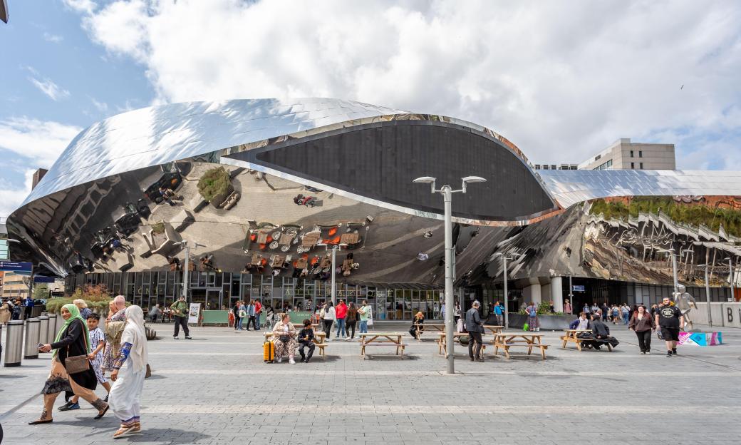 The modern, stainless steel entrance of Birmingham New Street railway station with pedestrians.