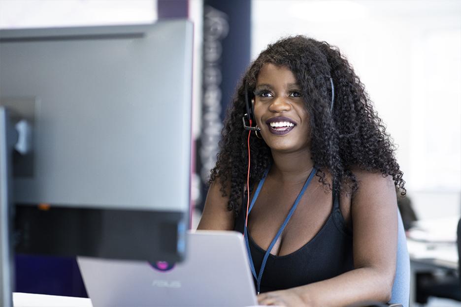 A woman with a headset working at a desk with a laptop.