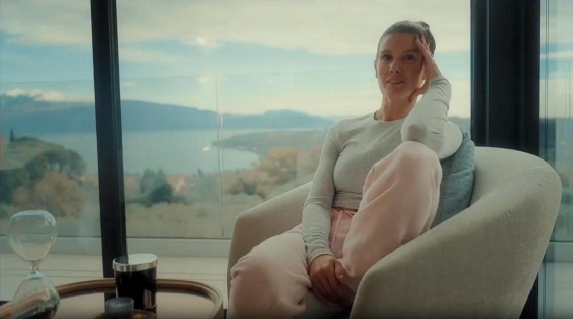Rebekah Vardy sitting in a chair with a view of a lake and mountains.
