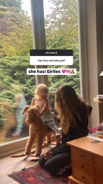 Zara McDermott with a toddler on a rocking horse in front of a window.