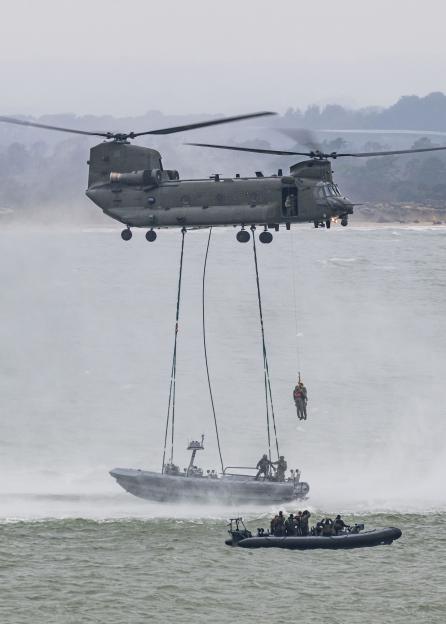 A Chinook helicopter winching a commando from a rigid inflatable boat (RIB) as another RIB full of commandos watches nearby, during a NATO training exercise.
