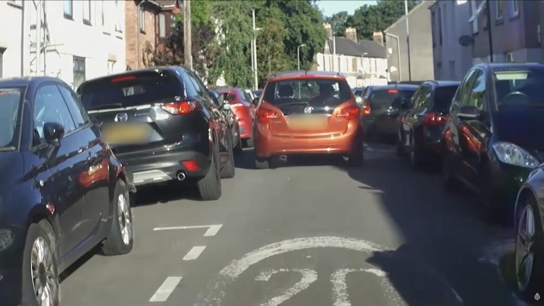 A street scene with multiple cars parked and driving, including an orange car that police boxed in to arrest a suspect.