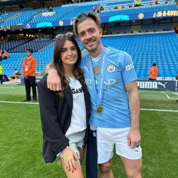 Sasha Attwood and Jack Grealish pose on the pitch at a stadium.