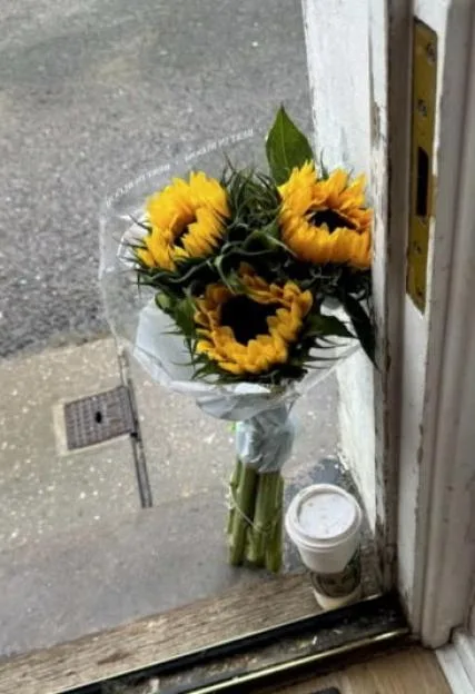 A bouquet of sunflowers resting on a doorstep next to a takeaway coffee cup.