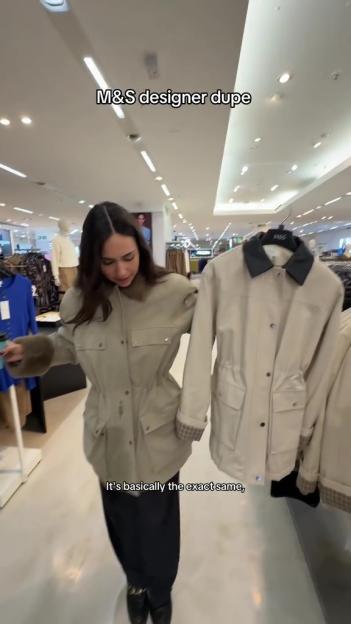 Woman in a department store comparing a coat she's wearing to a similar coat on a hanger.