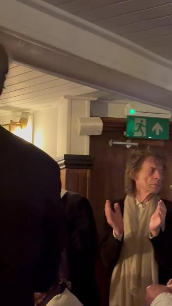 Mick Jagger singing in a pub, with his hands up, facing a crowd.