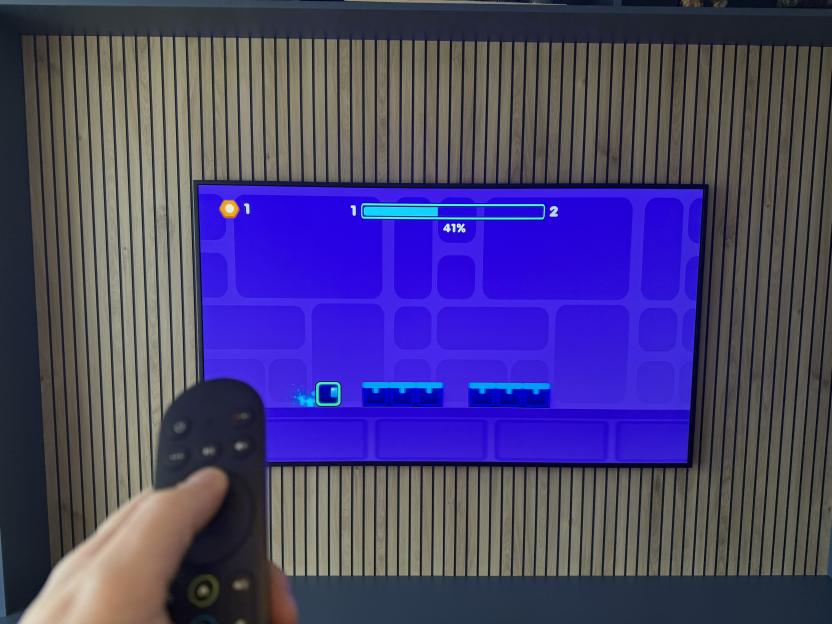 A person playing a video game on a TV with a remote control, displaying a bright blue game screen with a character and progress bar.