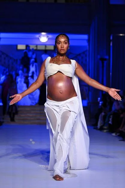 Leigh-Anne Pinnock walking the runway at the Di Petsa show during London Fashion Week, wearing a white outfit that exposes her baby bump.