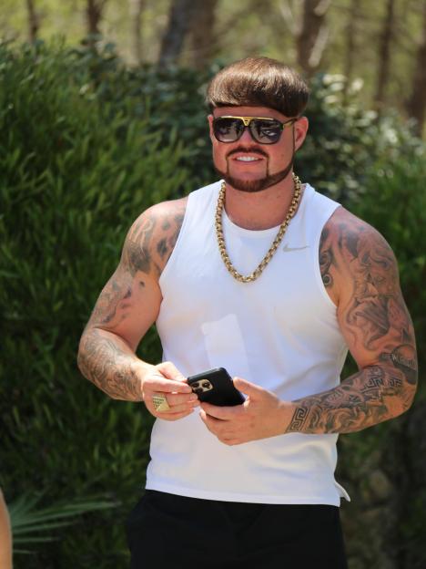 Jack Kay with a gold chain, sunglasses, and tattoos, holding a phone.