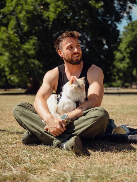 Sam Thompson holding his white cat in a park.