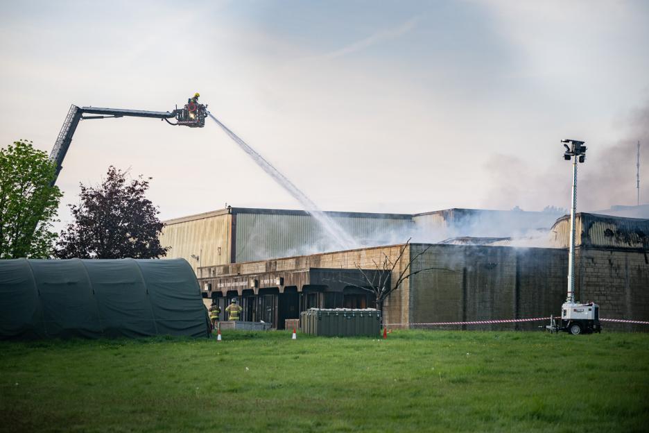 Firefighters tackling a blaze at a former commissary building, with a collapsed roof and smoke rising.