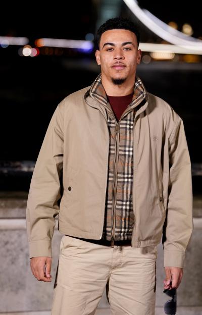 Morgan Rogers at London Fashion Week, wearing a beige jacket over a quilted plaid jacket and a maroon sweater, with beige pants.