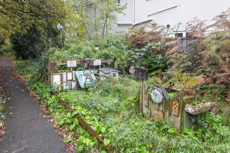 A footpath transformed into a "secret garden" with award plaques, a wheelbarrow, and diverse plants.