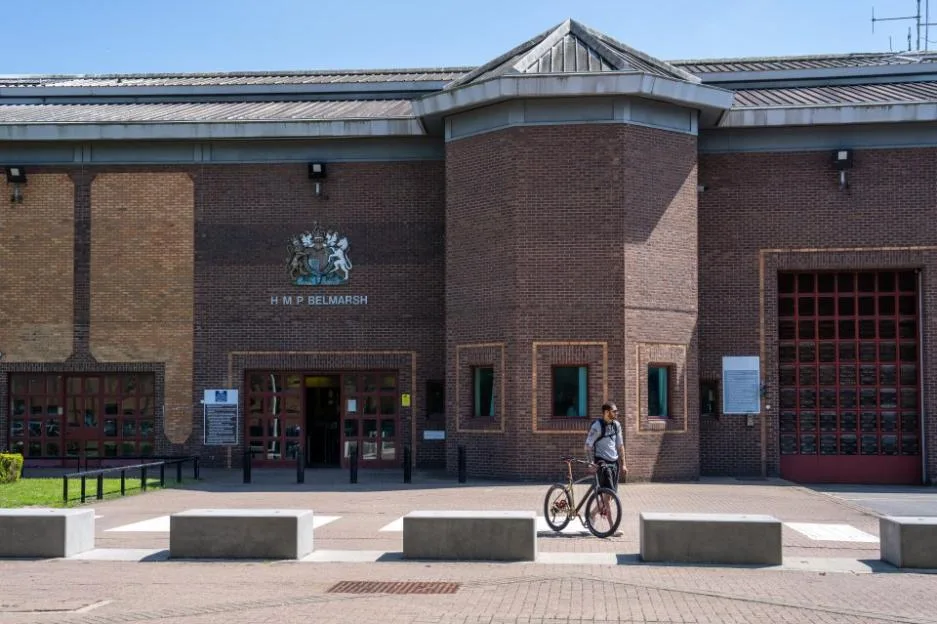 A man pushes his bicycle past the brick exterior of HMP Belmarsh prison.