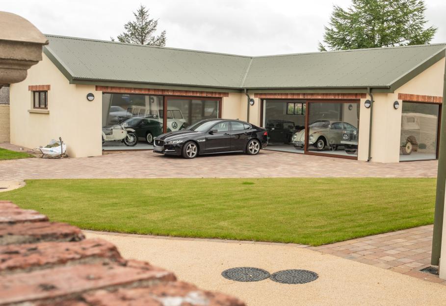 Margaret Loughrey's new house in Strabane, with a black sedan parked outside and various vintage cars visible through the garage windows.