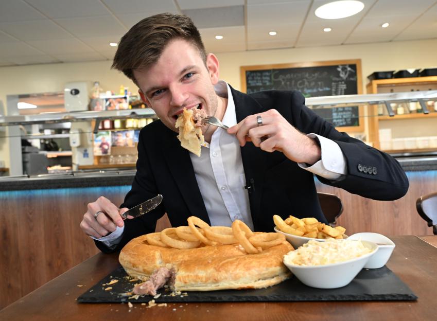 A man eating a large sausage roll with onion rings and chips from Countrystyle Meats Farmshop.
