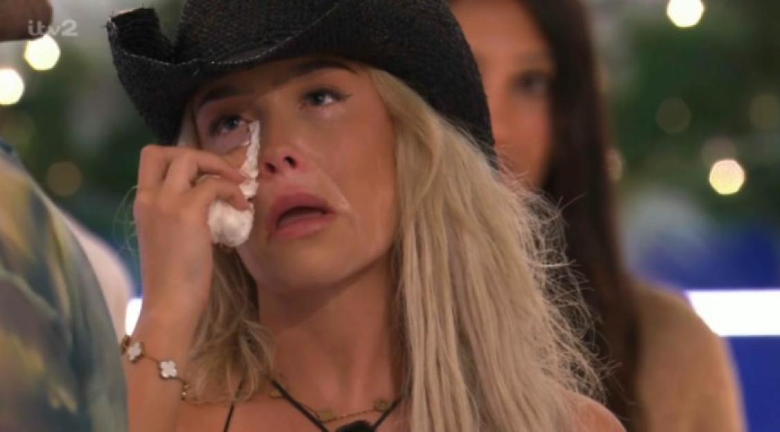 Woman crying while wearing a black cowboy hat and holding a tissue to her eye.