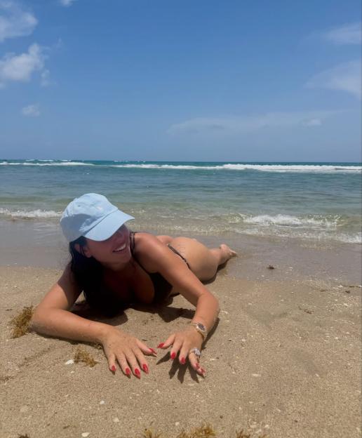 Georgina Rodriguez lying on a beach wearing a bikini and a light blue baseball cap.