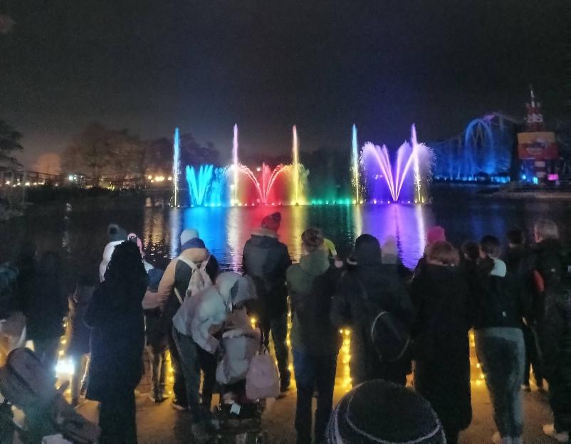 People watching a colorful light and fountain show over a body of water at Drayton Manor.