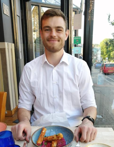 Tom Davies, a rugby player diagnosed with MND, seated at a restaurant table with food, smiling at the camera.