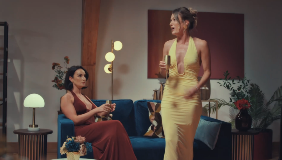 April storming off the reunion in a yellow dress while the other woman watches from a blue couch.