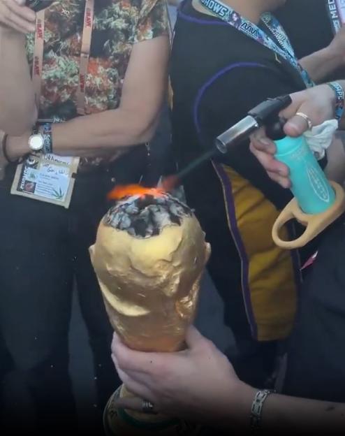 A person uses a torch lighter to ignite a massive joint shaped like the World Cup trophy.