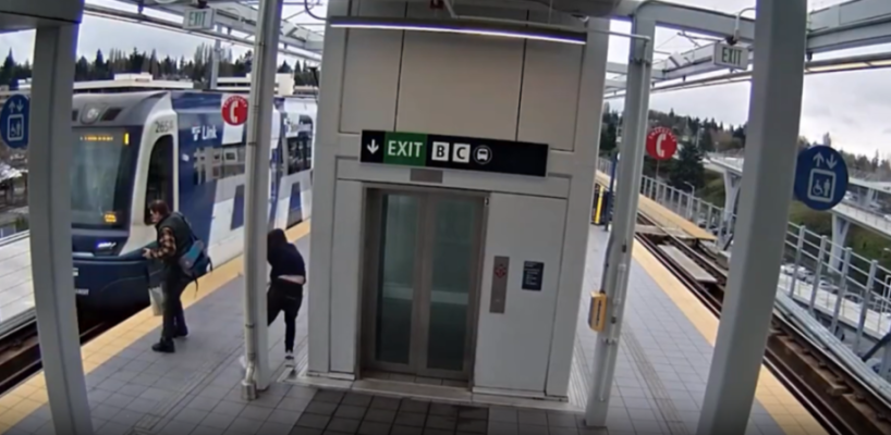A man wearing a backpack turns toward an oncoming train as another person behind him ducks away.