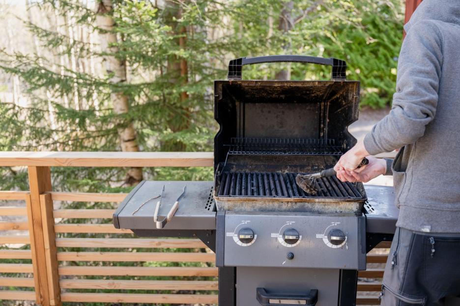 A person cleaning an outdoor barbecue grill with a wire brush.