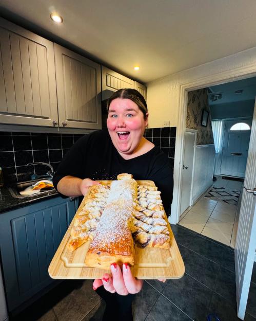 Becky Jones holding a large pastry dessert with powdered sugar.
